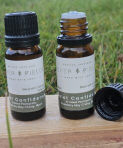 Two amber glass bottles of Quiet Confidence essential oil standing together. One bottle is closed with its black cap on and the other is open showing the dropper top.