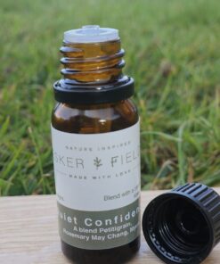 An open amber glass bottle of Quiet Confidence essential oil resting on a piece of natural wood laid on green grass.
