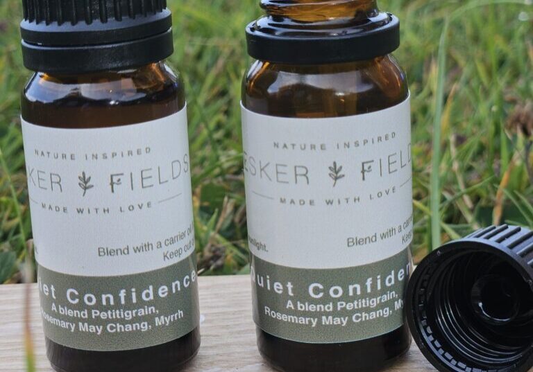 Two amber glass bottles of Quiet Confidence essential oil standing together. One bottle is closed with its black cap on and the other is open showing the dropper top.